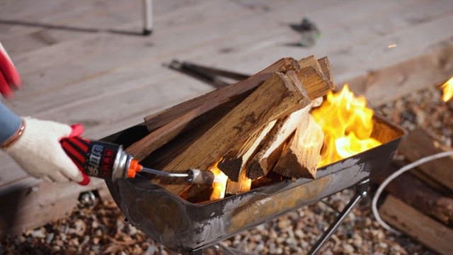 Person Igniting a Firewood Using a Torch