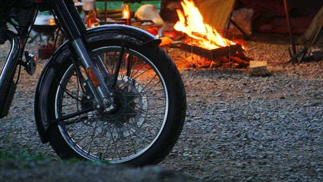 Motorcycle parked beside a campfire in a gravel lot at dusk
