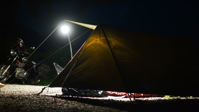Dark night camping scene with a motorcycle and a tent illuminated by a bright light