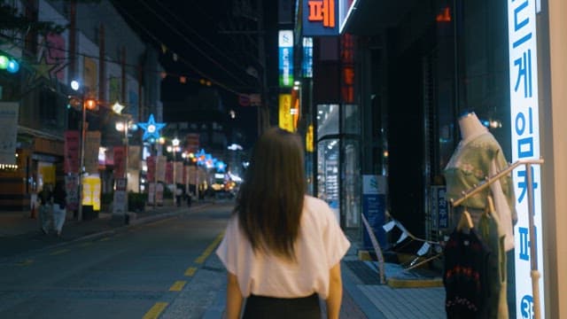 Woman walking through a neon-lit street at night