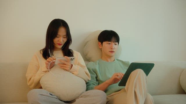 Two people using digital devices on a sofa in cozy living room