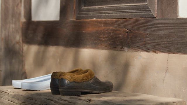 Rubber shoes and fur shoes placed in front of a rural house