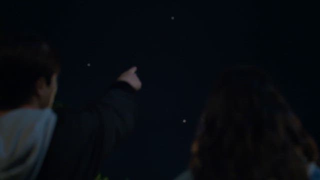 Two people pointing at stars in the night sky outdoors