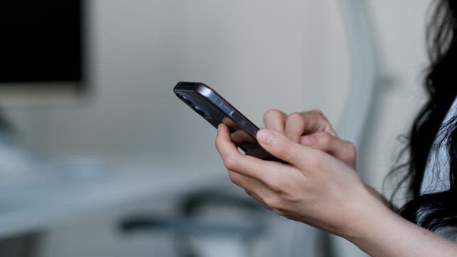 Woman with Black Long Hair Using a Mobile Phone in a White Room in front of a Desk