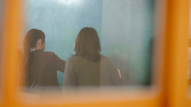 Students scribbling on the classroom blackboard viewed from outside the window