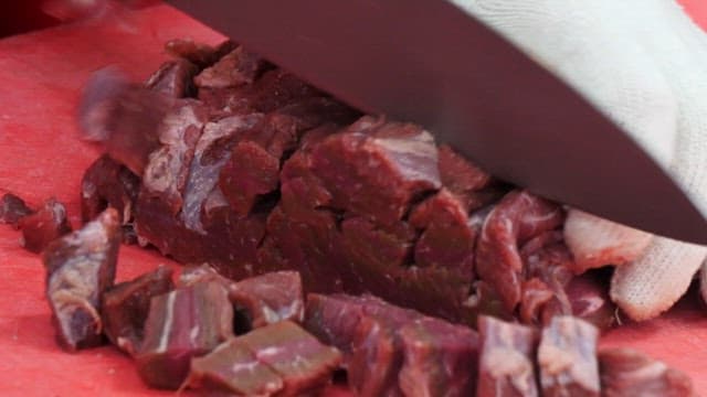 Person chopping beef on a red cutting board