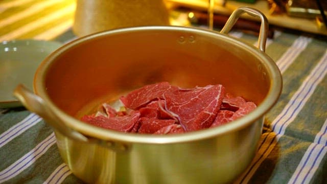 Gloved hands mixing meat and seasoning in a nickel-silver pot