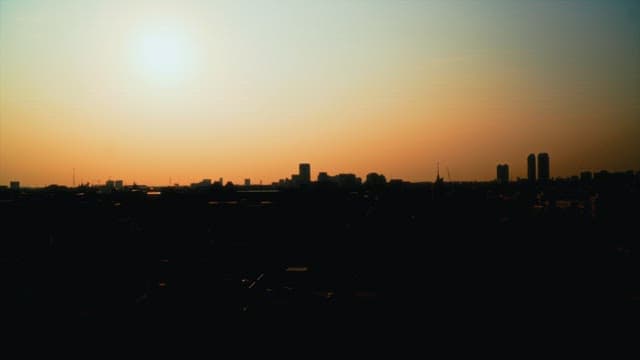 Sun setting over city skyline transitions to evening.