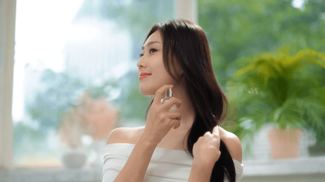 Woman spraying perfume indoors with a smile