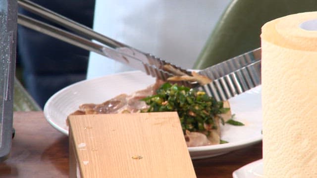 Wrapping spinach salad around pork with tongs