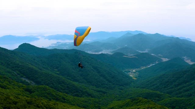 Paraglider soaring above scenic green mountains