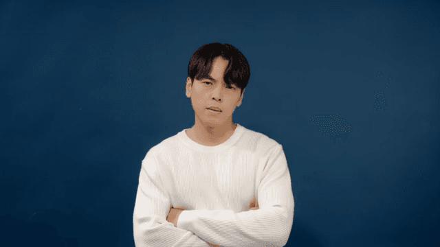 Man in a white sweater with his arms crossed and a serious expression shaking his head