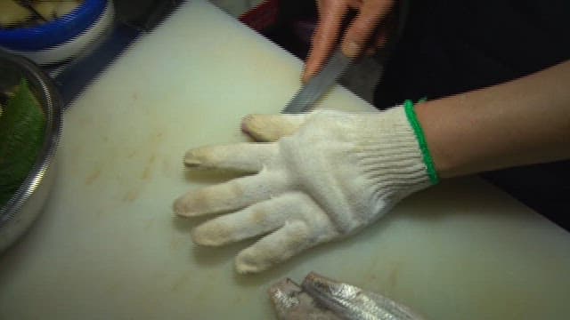 Sliced raw scaled sardine being prepared on a cutting board in a sushi restaurant kitchen