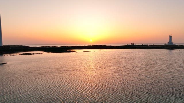 Sunset over a calm ocean with a lighthouse