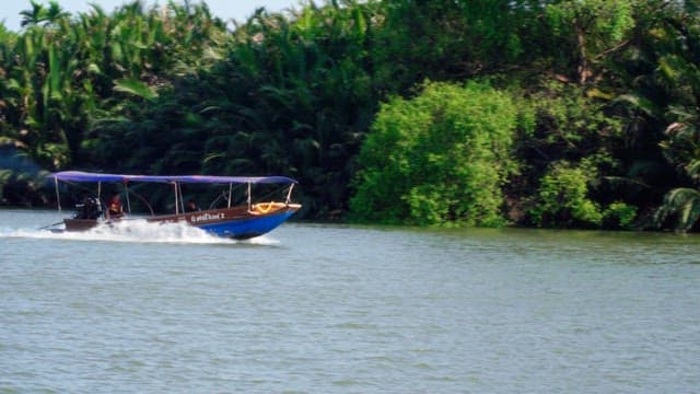 Boat sailing along a river next to a village and a green tropical forest