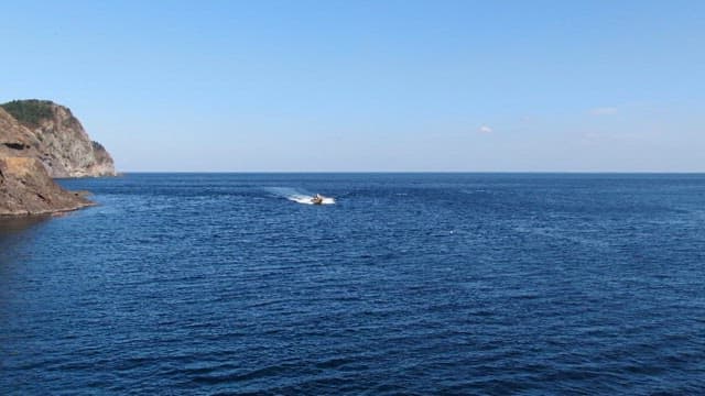 Boat Navigating Past Coastal Cliffs