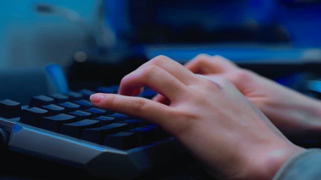 Hands typing rapidly on a backlit keyboard