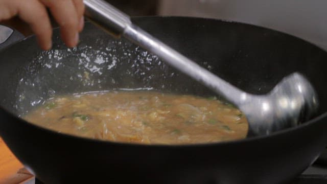 Using a ladle to pour egg stew cooked in a wok into a bowl