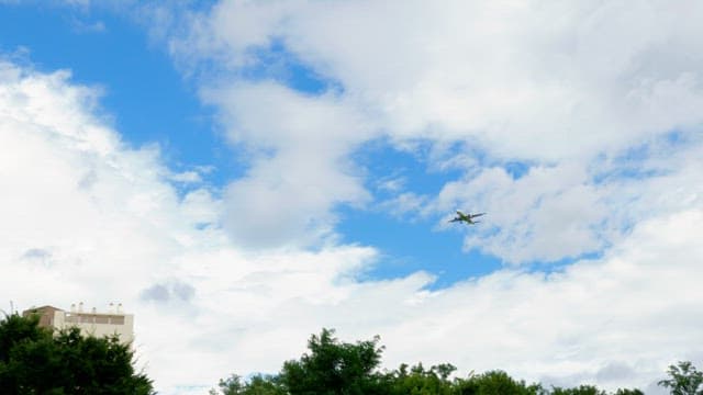 Airplane flying between clouds in clear sky