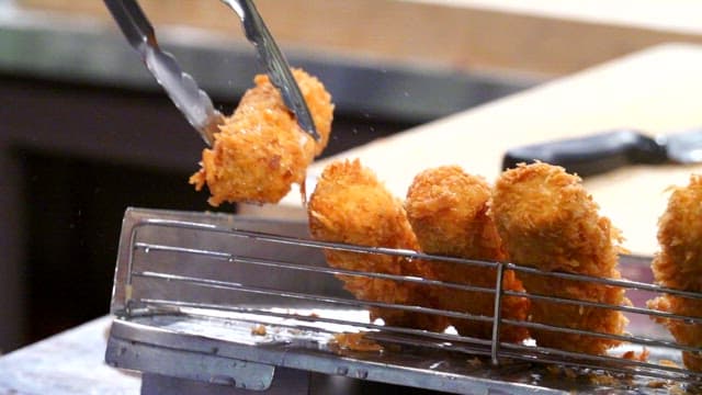 Crispy pork cutlet fried in deep fryer being lifted with tongs