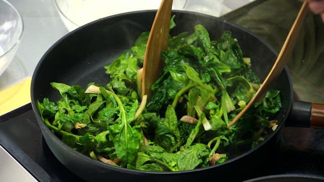 Stir-frying fresh spinach with wooden spatula in a pan