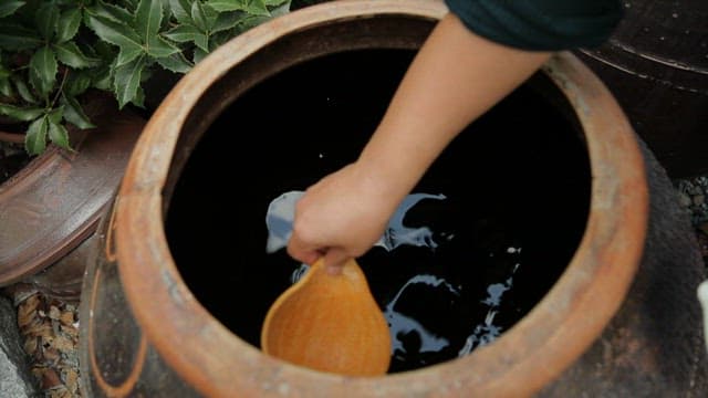 Soy sauce being poured into a ladle from a traditional Korean jar