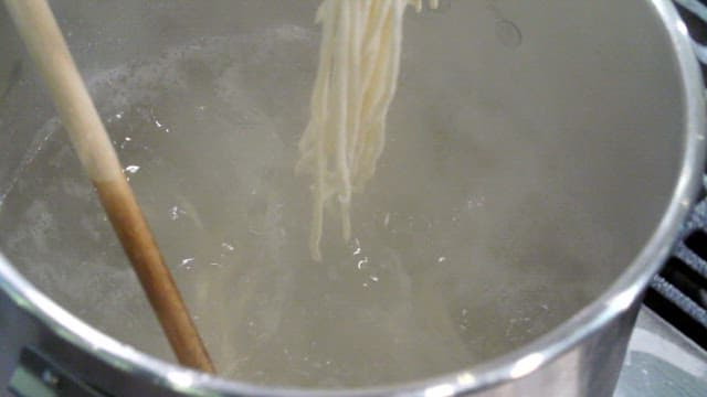 Udon noodles boiling in a pot with steam