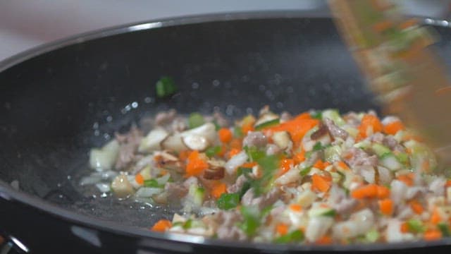 Person stir-frying chopped vegetables in a pan indoors