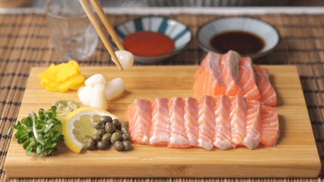 Eating rakkyo and capers on a wooden cutting board with salmon sashimi plated on it