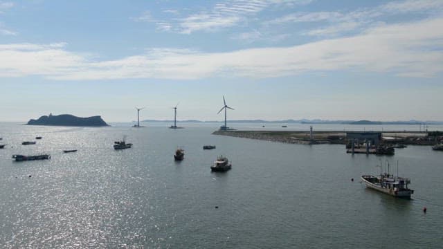 Boats on a serene ocean with wind turbines