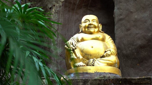 Golden Buddha statue seated in a rock cavity with surrounding green foliage