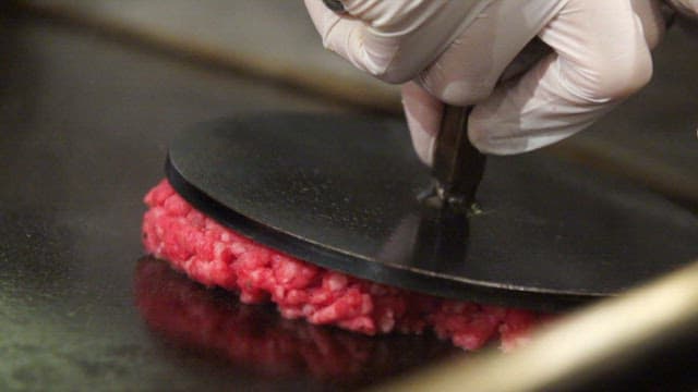 Pressing a raw beef patty on a grill
