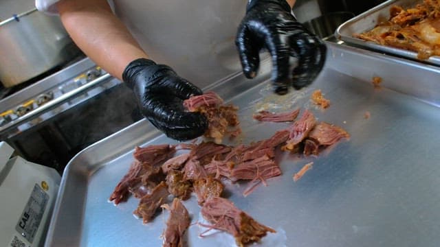 Preparing boiled meat on a metal tray with gloved hands