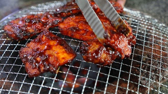 Meat sizzling on a grill over blazing charcoal