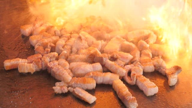 Grilling juicy pork belly on a hot plate with roaring flames