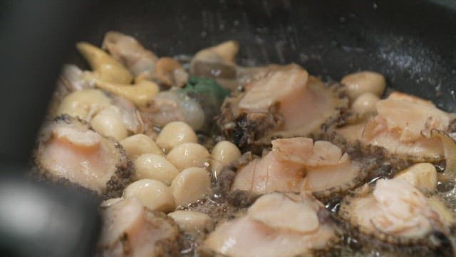 Fresh abalone being cooked with garlic in a pan.