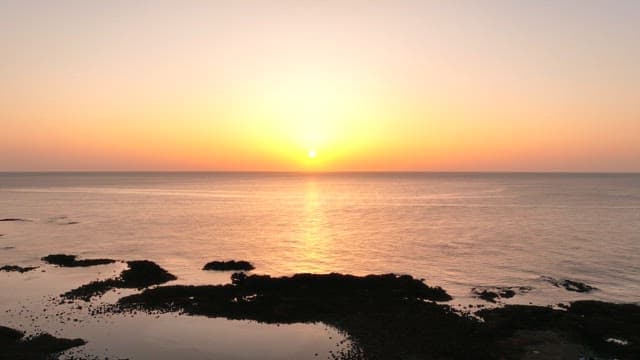 Sunset over a calm ocean with rocky shore