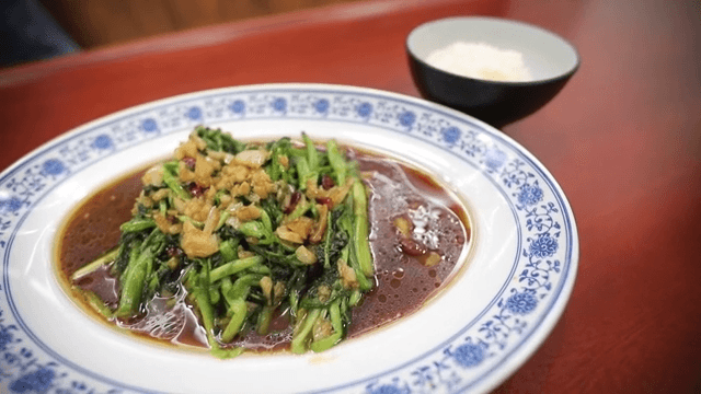 Plate of stir-fried water parsley and a bowl of rice on a wooden table