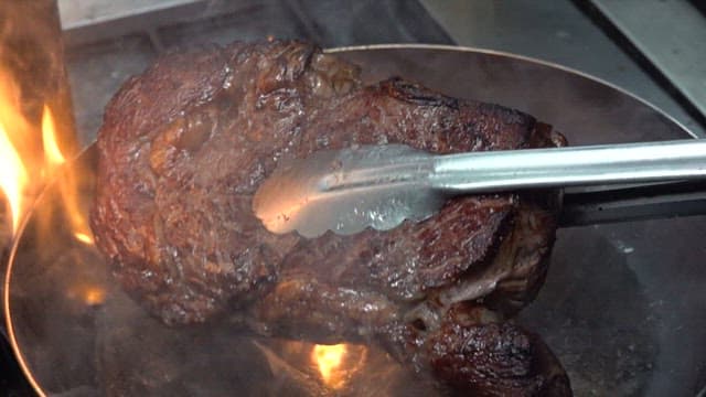 Cooking a steak on a flaming pan with tongs