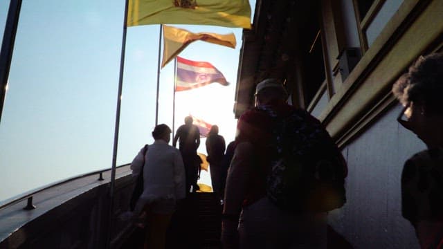People walking up stairs with Buddhist temple flags waving in the morning sunlight