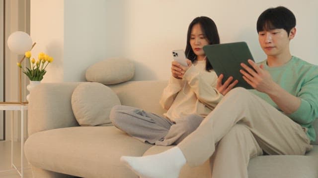 Two people using digital devices on a sofa in cozy living room