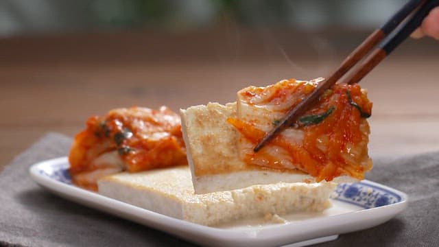 Person using chopsticks to pick up kimchi and tofu