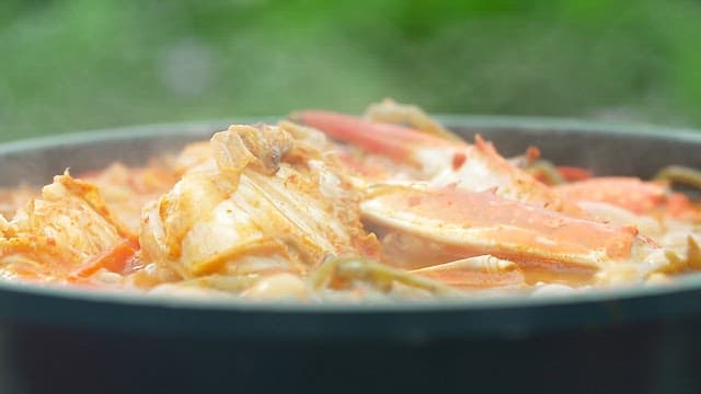 Chopsticks lifting sweet potato stem from boiling crab soup