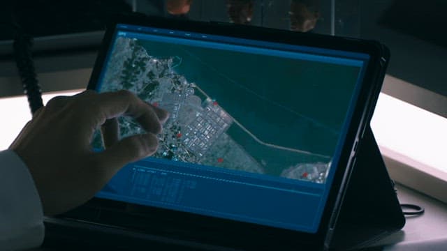 Person using a tablet to examine detailed satellite maps in a dimly lit room