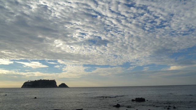 Serene coastal scene with island at sunrise and sky with white clouds