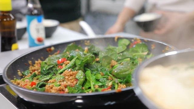 Stir-frying spinach and rice in a hot pan in a kitchen