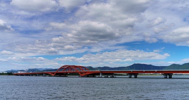Red bridge over a river on a cloudy day with mountains in the background.