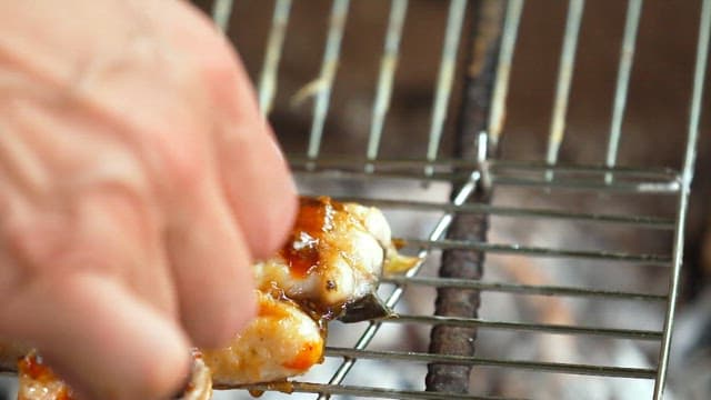 Applying sauce to eel grilled over charcoal