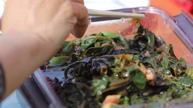Chopstickful of appetizing and salty pickled spinach in a container