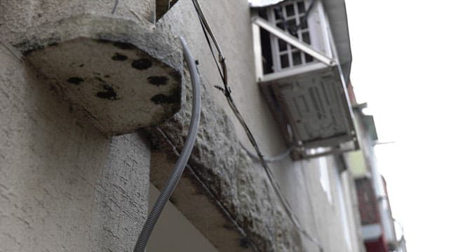 Exterior wall with old air conditioner and cables in the rain